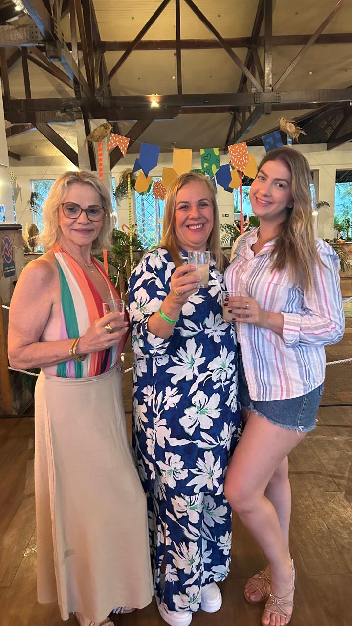 Três amigas brindando em salão decorado com bandeirolas.