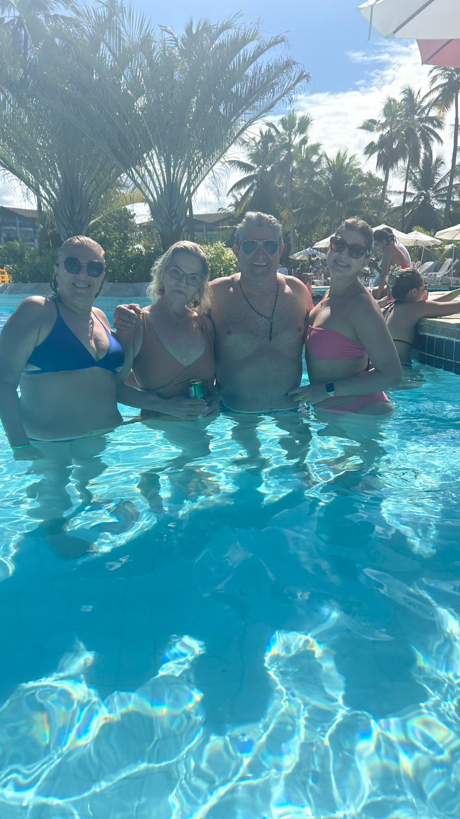Quatro amigos posando dentro da piscina com palmeiras ao fundo.