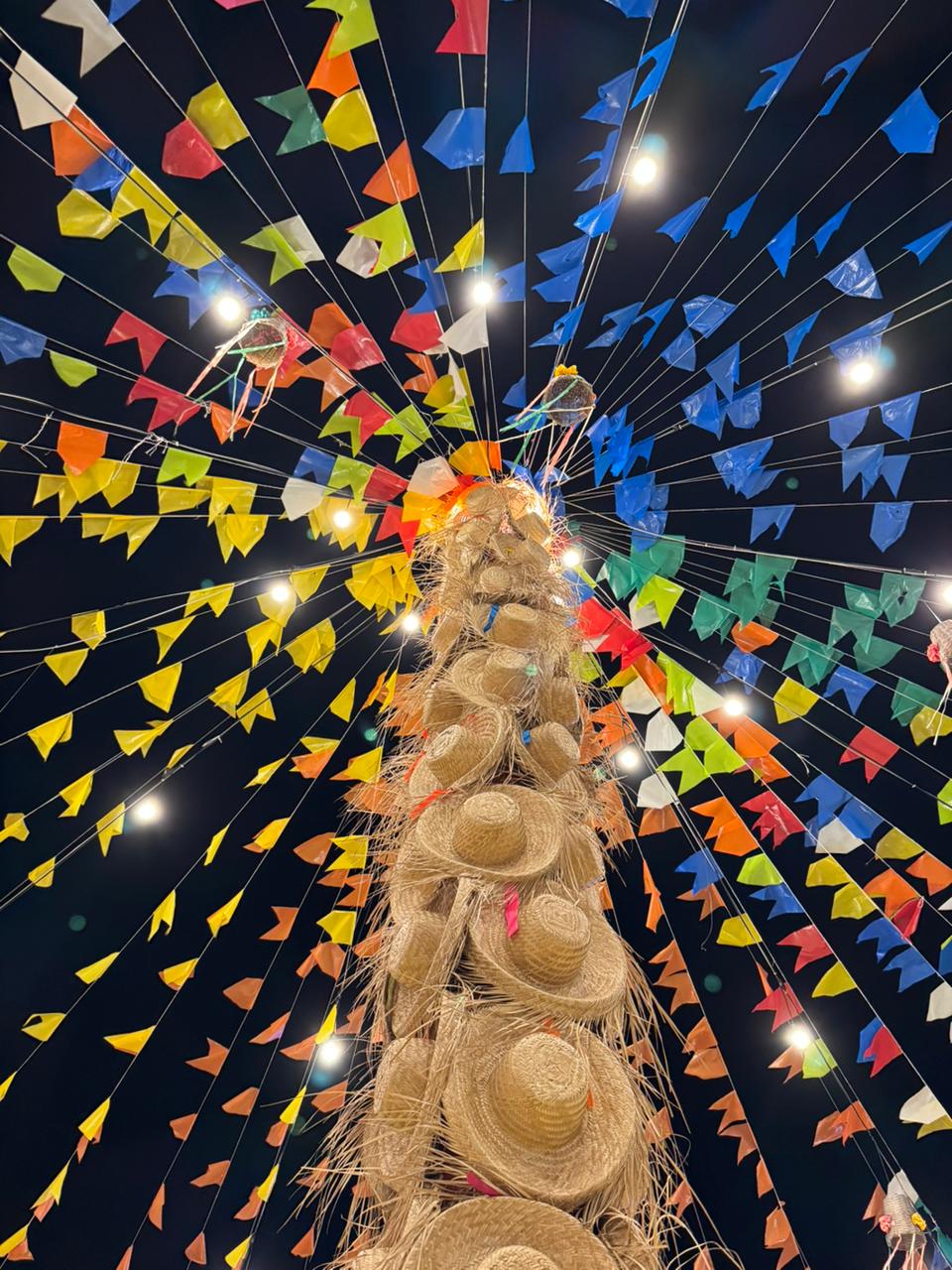 Bandeirolas e chapéus decorativos iluminados sobre a praça da Vila.